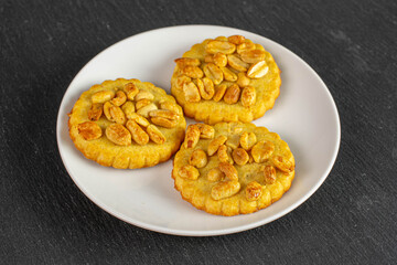 Group of three whole delicious cookie with peanuts on white ceramic plate on grey stone
