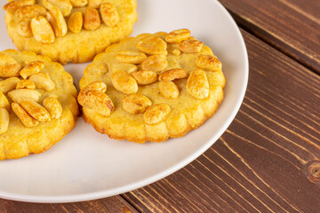 Group of three whole delicious cookie with peanuts on white ceramic plate on brown wood