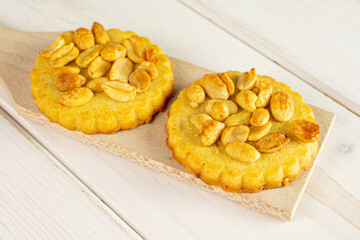 Group of two whole delicious cookie with peanuts on small wooden cutting board on white wood