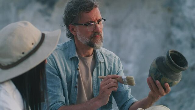Mature archaeologist discussing antique vessel with colleague