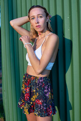 Young woman with short blond hair with green corrugated metal fence behind in summer