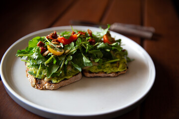 Healthy toast with avocado, arugula and sun dried tomatoes on rustic wooden table.