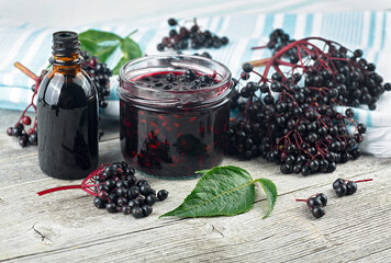 Delicious homemade black elderberry syrup in glass jar and bunches of black elderberry with green...