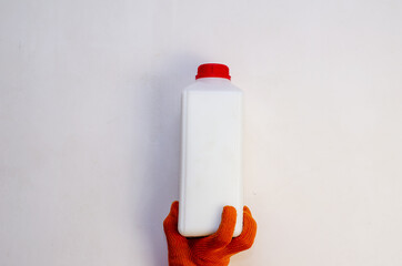 A hand in a red protective glove holds a plastic container against a light background. A man's hand...