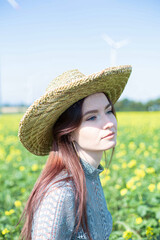 White girl with dark hair in straw hat with sky behind in meadow