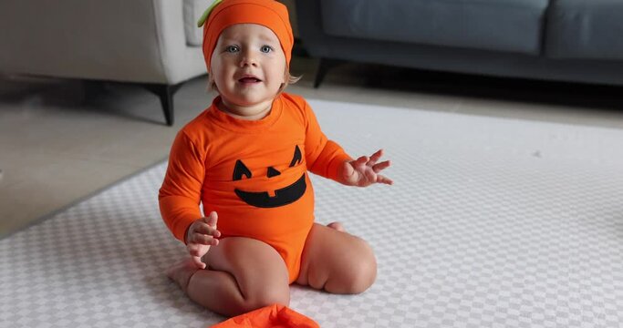 Cute Caucasian baby girl one year old in orange clothing and hat having fun and celebrating Halloween at home during Coronavirus covid-19 pandemic and quarantine. Slow motion