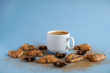 White cup of coffee spiced with cinnamon near brown cookies and star anise