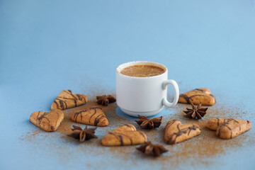 White cup of coffee spiced with cinnamon near brown cookies and star anise