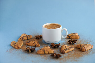 White cup of coffee spiced with cinnamon near brown cookies and star anise