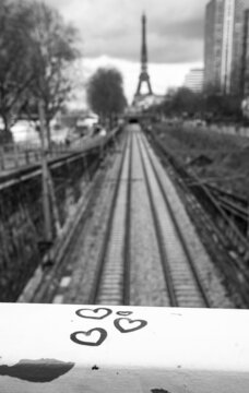 Parisian urban romantics. Hearts on the bridge railing with view railway and Eiffel tower at background. Black white historic photo.