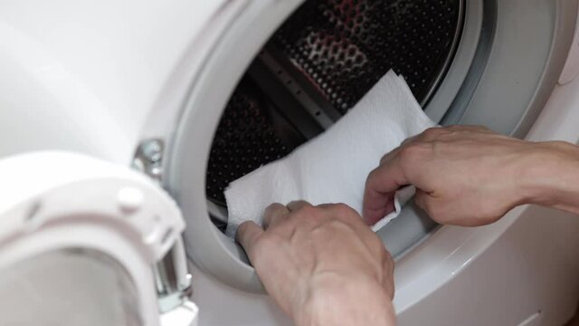 Hands cleaning moisture from the washing machine drum. Washing machine maintenance concept