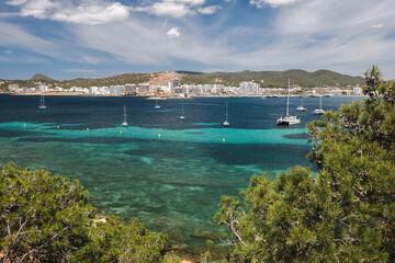 Fototapeta na wymiar Bay of Ibiza coastline with turquoise water and yachts on sunny summer day. View to the Port de Sant Antoni de Portmany