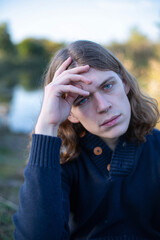 Young european man with long hair with lake behind with blue eyes