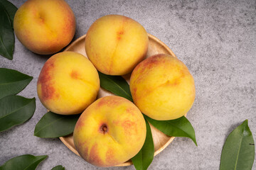 Golden Yellow Peach in wooden plate on gray background.