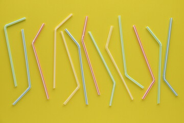 Disposable plastic straws on yellow background.