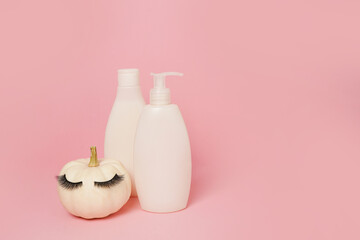 pumpkin with false eyelashes and mock up cosmetic containers shampoo or gel on pink background,...