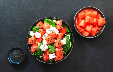Watermelon salad bowl with feta cheese, spinach and black sesame seed, dark background, top view, copy space