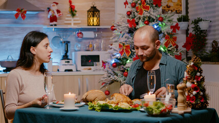 Man and woman enjoying festive dinner on christmas in decorated kitchen. Cheerful couple celebrating winter holiday with traditional food and glasses of champagne. People with seasonal meal