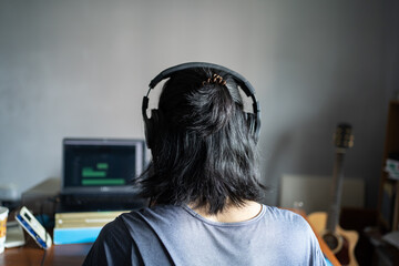 A man with long hair wearing headphones and sitting in front of laptop computer. Musician working...