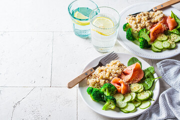 Quinoa, salted salmon, cucumber and broccoli on white plate, gray tile background. Healthy food...