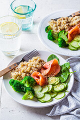 Quinoa, salted salmon, cucumber and broccoli on white plate, gray tile background. Healthy food concept.