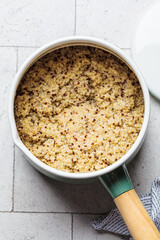 Cooked quinoa in saucepan, gray tile background, top view.