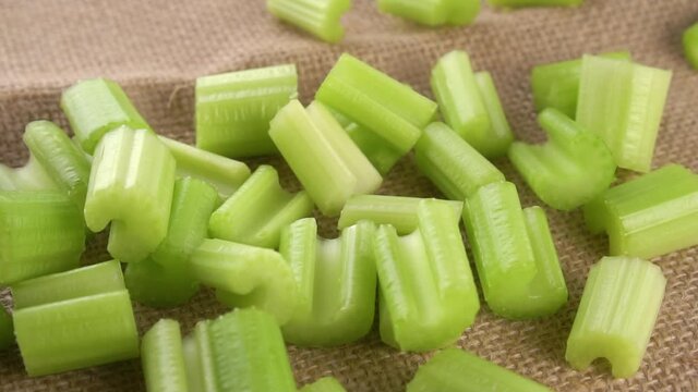 Slices chopped fresh celery stalk falling on a burlap rough tablecloth. Macro. Slow motion. Rustic view. Rotation