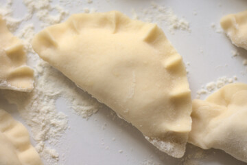 Uncooked, homemde, Polish dumplings (pierogi) lying on a white kitchen counter.