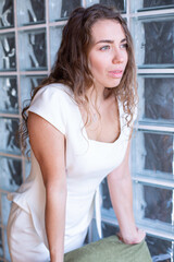 European girl with curly hair with windows behind in white suit