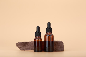Two skin serum bottles next to natural stone against beige background with copy space. Concept of...