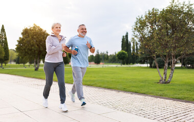 Full-length photo of lovely joyful retirees couple jogging outside in city park