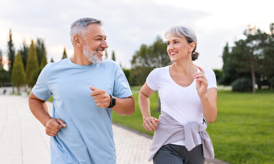 Happy senior husband and wife in sportive outfits running outdoors in city park