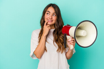 Young caucasian woman holding a megaphone isolated on blue background relaxed thinking about something looking at a copy space.