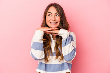 Young caucasian woman isolated on pink background keeps hands under chin, is looking happily aside.