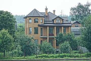 large brown brick private house among green vegetation and trees on the street