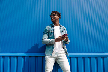 Black guy with a phone in his hands on the background of a blue building, writes sms to the phone