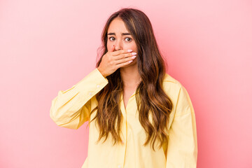 Young caucasian woman isolated on pink background covering mouth with hands looking worried.