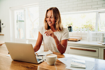 Caucasian female student typing on laptop smiling while on video call with class mates 