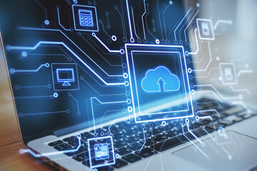 Close up of laptop at desktop with abstract glowing circuit cloud computing interface on blurry blue bokeh background. Information, technology and network concept.