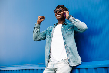 successful american black guy calls on the phone, shows a sign of success and joy to victory, on a...