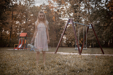 Ghost teen girl in white dress with dirty toy near a empty playground. Holiday event halloween...