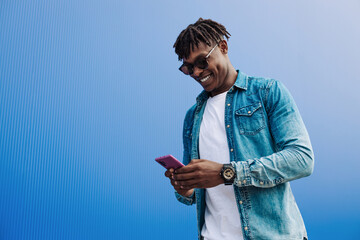 african man in sunglasses typing sms over blue background, 5g internet concept, high speed internet...
