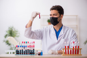 Young male biochemist testing blood samples in pandemic concept