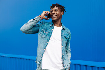 african man calling on the phone on blue background, 5g internet concept, high speed internet on phone - obrazy, fototapety, plakaty