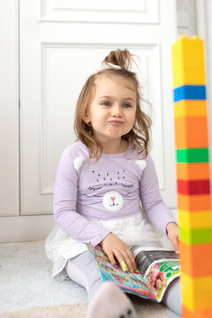 Surprised emotional little adorible child girl with big blue eyes siting on the floor in the children's room. Play with colored blocks. Lifestyle photo vertical