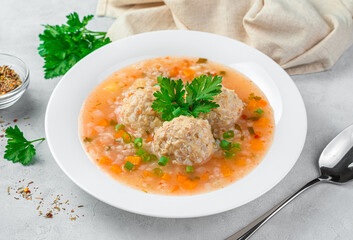 Healthy soup with turkey meat meatballs with vegetables in a white plate on a gray background.