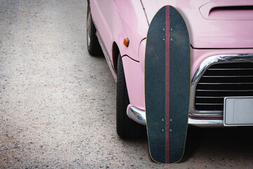 Old surfskate with pink vintage car on road in the parking.