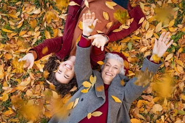 Poster Grandmother and granddaughter lying on foliage and enjoy the autumn © Rido