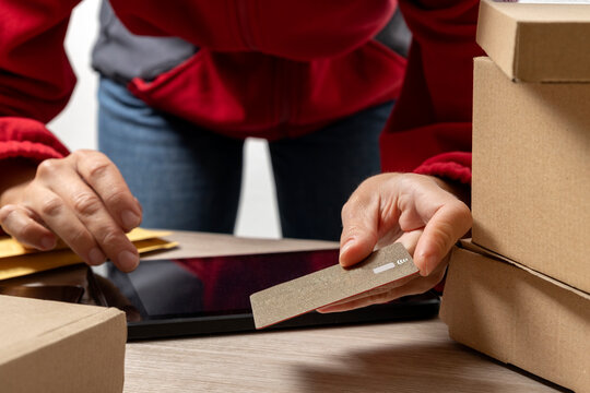 Closeup of delivery person wearing red jacket, using golen credit card and pc tablet for cheking and paying for order.Boxes,parcels,device,credit card on the desk