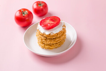 A stack of thin salty waffles with creamy sauce and tomato